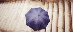 Blauer Regenschirm von oben, Person geht auf einer Treppe.